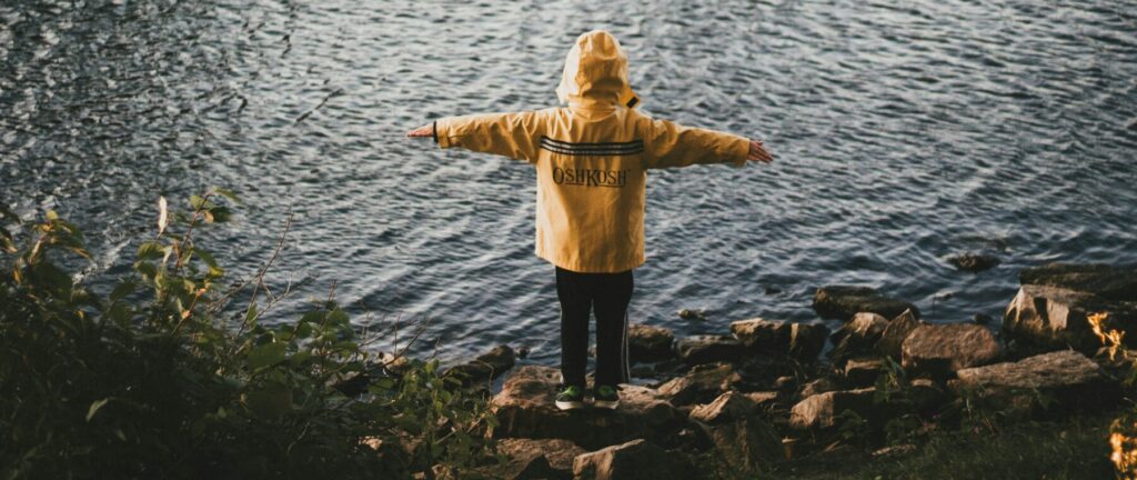 Child standing outside overlooking a lake filled with ducks.